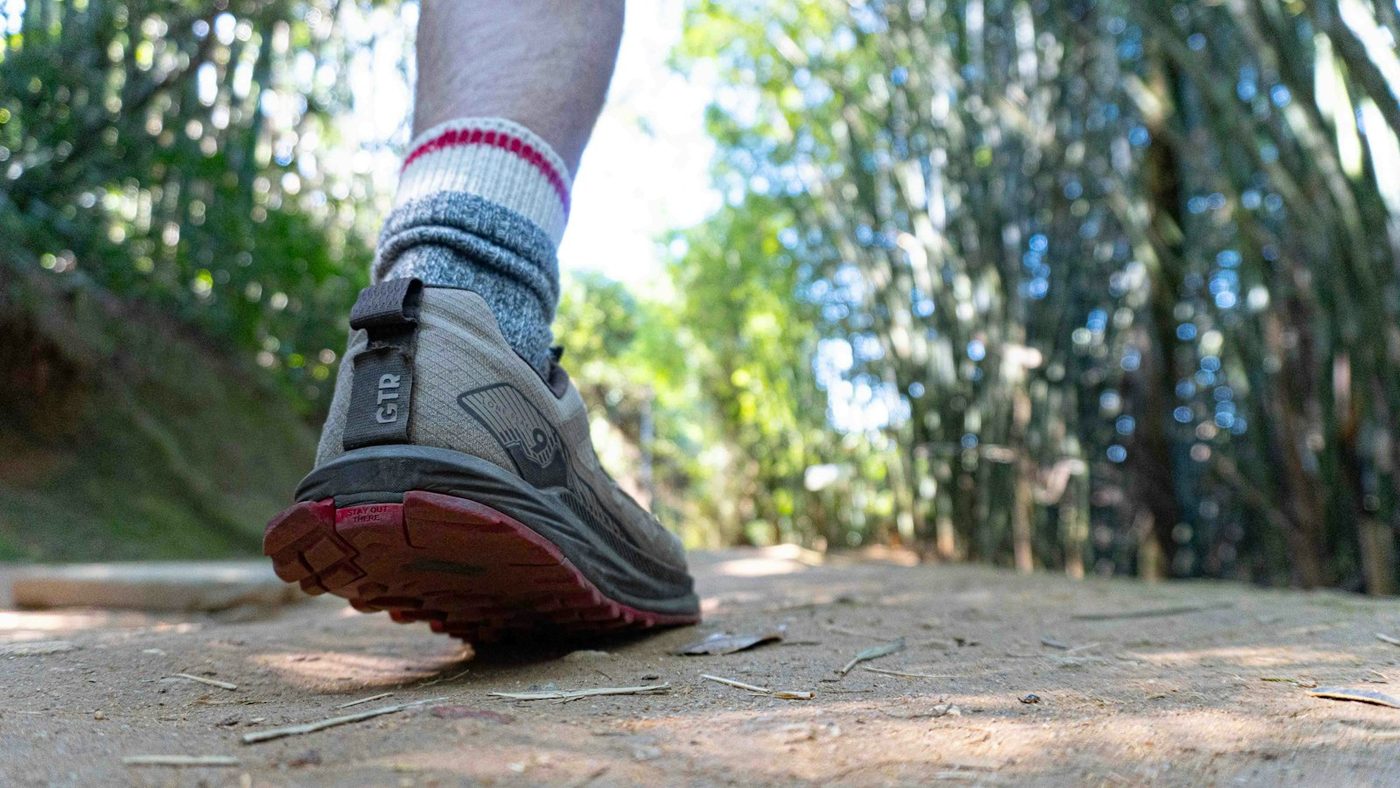 Trail running shoe and wool sock on a dirt path