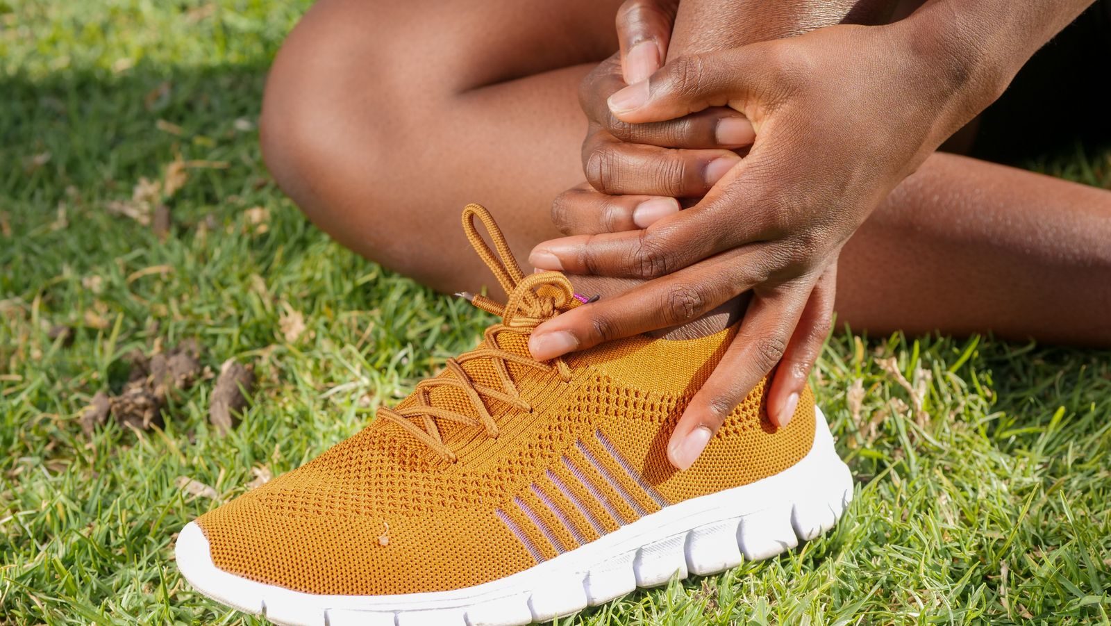 Runner sitting on grass holding their foot and ankle