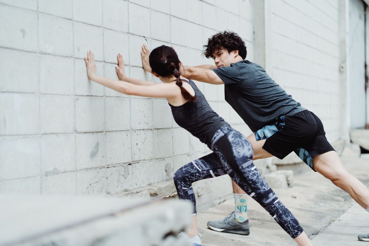 Two people doing a calf stretch against a wall